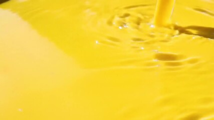Poster - Close-up view of pouring yellow liquid, creating ripples and splashes on the surface.