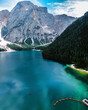 © AmazingAerialAgency - Aerial view of a serene turquoise lake mirroring rugged mountains and dense evergreen forests, a scene of tranquil beauty, Braies, Trentino-South Tyrol, Italy.