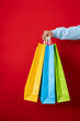 © Answer 7 - Male hand holding three multicolored shopping bags on a red background, shopping concept