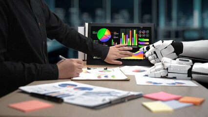 Poster - A human hand collaborates with a robotic hand in a contemporary office, analyzing colorful graphs and data visualizations to foster teamwork and innovation.Noogenesis