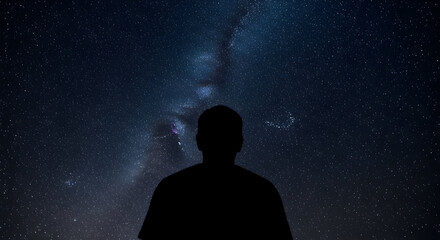 Silhouette of a person gazing at a stunning starry night sky with the Milky Way galaxy visible in the background creating a sense of wonder and exploration in the universe