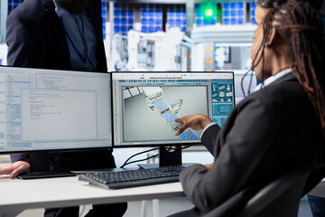 Poster - Programmer in photovoltaics factory office using PC to update software of robot arms placing solar panels on assembly lines, communicating changes to team leader, close up shot
