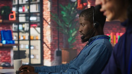 Poster - Call center coworkers dealing with upset customers, speaking with them online using headset at office desk. Asian man using PC to do customer support job, handling clients complaints, camera A