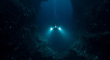 A submersible with bright lights descends into the deep blue ocean with dark rocky surroundings