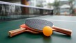 © Iaroslav - Table tennis rackets and ball lying on wooden ping pong surface, surrounded by green outdoor setting, ready for casual match