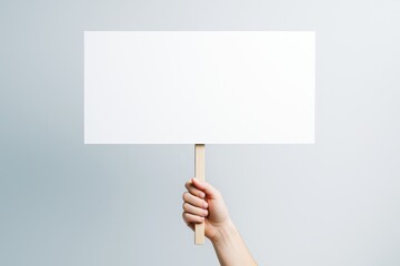 Poster - Hand holding blank white rectangular sign on stick against light gradient background for mockup, poster, promotion, or branding concept.