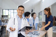 © SOMKID - A male doctor smiling looking at the camera in meeting room, Medical team reviewing data.