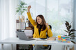 © Kritdanai - Business Success: A joyful woman exults in her office after a moment of accomplishment, her elation enhanced by the sleek laptop, the neat arrangement of work supplies, and the bright.