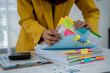© Kritdanai - Organizing the Data: A dedicated business professional meticulously organizes a vast collection of documents, meticulously arranging each file with colorful sticky notes and a calculator.