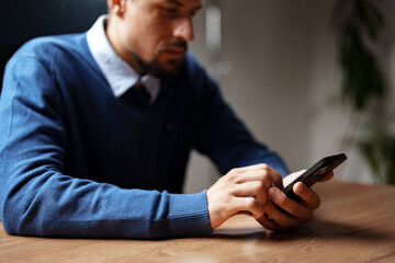 Poster - Man using smartphone while sitting at a wooden desk in a modern office during daytime