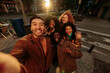 © bernardbodo - Group of happy multiracial friends taking photo of themselves in urban street during sunset
