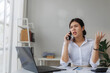 © Phimwilai - Stressed asian businesswoman arguing during phone call and working on laptop in office