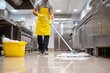 © The Little Hut - Professional cleaner in yellow apron mopping shiny kitchen floor in commercial food service environment with cleaning tools and stainless steel appliances