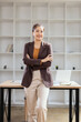 © SOMKID - young businesswoman standing arms crossed at desk in office.