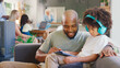 © Monkey Business - Father And Son Using Digital Tablet At Home With Multi-Generation Family In Background