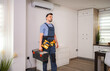 © Jelena - Technician walking in the apartment carrying a toolbox and looking at the air conditioner
