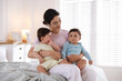 © New Africa - Happy mother with her cute little twin babies on bed indoors