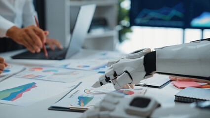 Poster - A robot arm collaborates with a human in a modern office, analyzing various graphs and data on a desk, illustrating the future of technology and teamwork.Noogenesis
