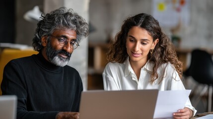 Poster - Two multiethnic professionals colleagues working together with laptop and papers in office. Indian male mentor and latin female young professional sitting in creative office space., no logos, no bran