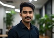 © sujon1638 - Portrait of a young indian man with a mustache wearing a dark collared shirt in a modern office environment