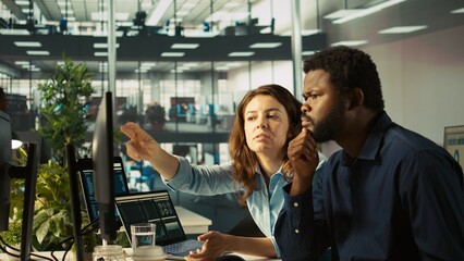 Poster - Employee and coworker looking over revenue figures on PC in office. Teamworking colleagues focused on comparing company statistical numbers, working hard to finish job before deadline, camera B