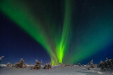 Stunning aurora borealis over Lapland night landscape. Bright green and purple northern lights dancing in the starry sky above snowy rural terrain. Long exposure photo of natural arctic phenomenon.
