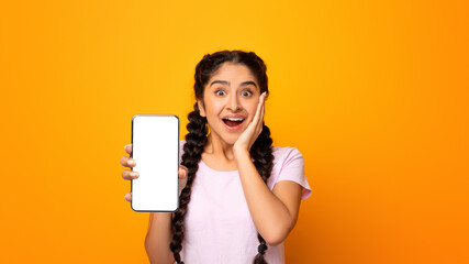 Amazing Useful App. Portrait of excited and surprised young indian woman holding smartphone with black blank screen in hand, showing device. Gadget with empty free space for mock up template