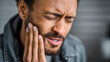© AdamDiezel - Man is touching his cheek and experiencing a toothache, blurred background.