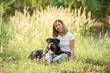 © sutlafk - Happy Asian woman sitting in a field with her Rottweiler dog, enjoying nature and sunshine. Concept of pet love, outdoor lifestyle, and peaceful countryside moments.