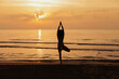 © Dina - silhouette of young woman on the beach at sunrise, doing yoga, standing in meditation tree position, doing breathing and balance exercise. Healthy lifestyle.
