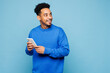 © ViDi Studio - Young man of African American ethnicity wear sweatshirt casual clothes hold in hand use mobile cell phone look aside isolated on plain pastel light blue background studio portrait. Lifestyle concept.