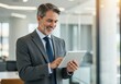 © sujon1638 - Professional businessman with graying hair and beard confidently uses a tablet device in a modern office setting