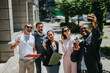 © qunica.com - A group of cheerful and diverse business coworkers taking a selfie together outdoors, showcasing teamwork and camaraderie in an urban environment.