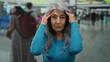 © Krakenimages.com - Senior woman with grey hair in blue sweater expressing frustration in an indoor airport terminal with blurred travelers in the background.