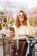 © maxbelchenko - A cheerful tourist with a phone in her hands rides a bicycle on a sunny day in the park. A young woman enjoys a walk at sunset, blogs or texts on her phone. Blogging, tourism concept.