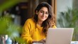 © Johannes - Smiling indian young adult woman wearing glasses typing on laptop computer working at home office sitting at table. Happy female professional freelancer student studying online using notebook pc., no
