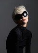 © SHOTPRIME STUDIO - Elegant young woman with short platinum hair wearing oversized black sunglasses and a black turtleneck, posed against a dark grey background. Fashion and style concept.