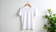© RatihMeiriga - A white t-shirt hangs on a wooden hanger against a white wall, with a green plant on the right.