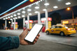 © UniDesign by Sonjib - Person holding smartphone at a brightly lit gas station at night