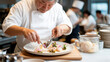 © mandm. - Chef carefully arranges gourmet dish featuring edible flowers on white plate, creating refreshing and artistic presentation in professional kitchen setting