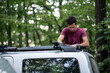 © Zoran Jesic - Man installing roof rack on car in forest: preparing for adventure