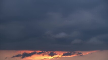 Wall Mural - A timelapse video captures a dramatic sunset sky transitioning from vibrant orange and yellow hues near the horizon to deep blue and purple clouds above, creating a stunning and serene atmosphere.
