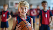 © Julia Zarubina - Smiling blond boy 10 years old in basketball uniform holding basketball ball in the center of school gym, other children in sports uniform behind, physical education lesson, game, team, training