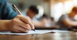 © Marina Demidiuk - Close-up of a hand holding a pen and paper, doing an exam in school, writing something. Blurred background. The student is sitting at their desk, taking a mental test for a final-year class.