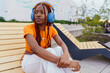 © Iryna - Young Black woman wearing headphones sitting on urban bench, looking sideways