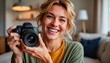 © Татьяна Блуднева - Smiling young woman holding a camera indoors in cozy living room