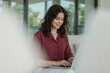 © Masud - Young woman smiling while working on a laptop in a bright modern setting
