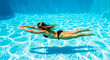 © rnroni - Woman swimming underwater in a clear blue swimming pool with sunlight reflections