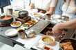 © Masakazu Tokashiki - In a kalbi barbecue restaurant, a server grills a cut of meat over glowing coals, flames licking edges as steam rises from sizzling fat, filling the air with rich aroma. Seoul, Jung District, spring.