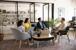 © fizkes - Group of corporate staff members participate in briefing gathered in modern coworking office lobby, discussing marketing campaign, review new project details and improvements, share ideas and solution